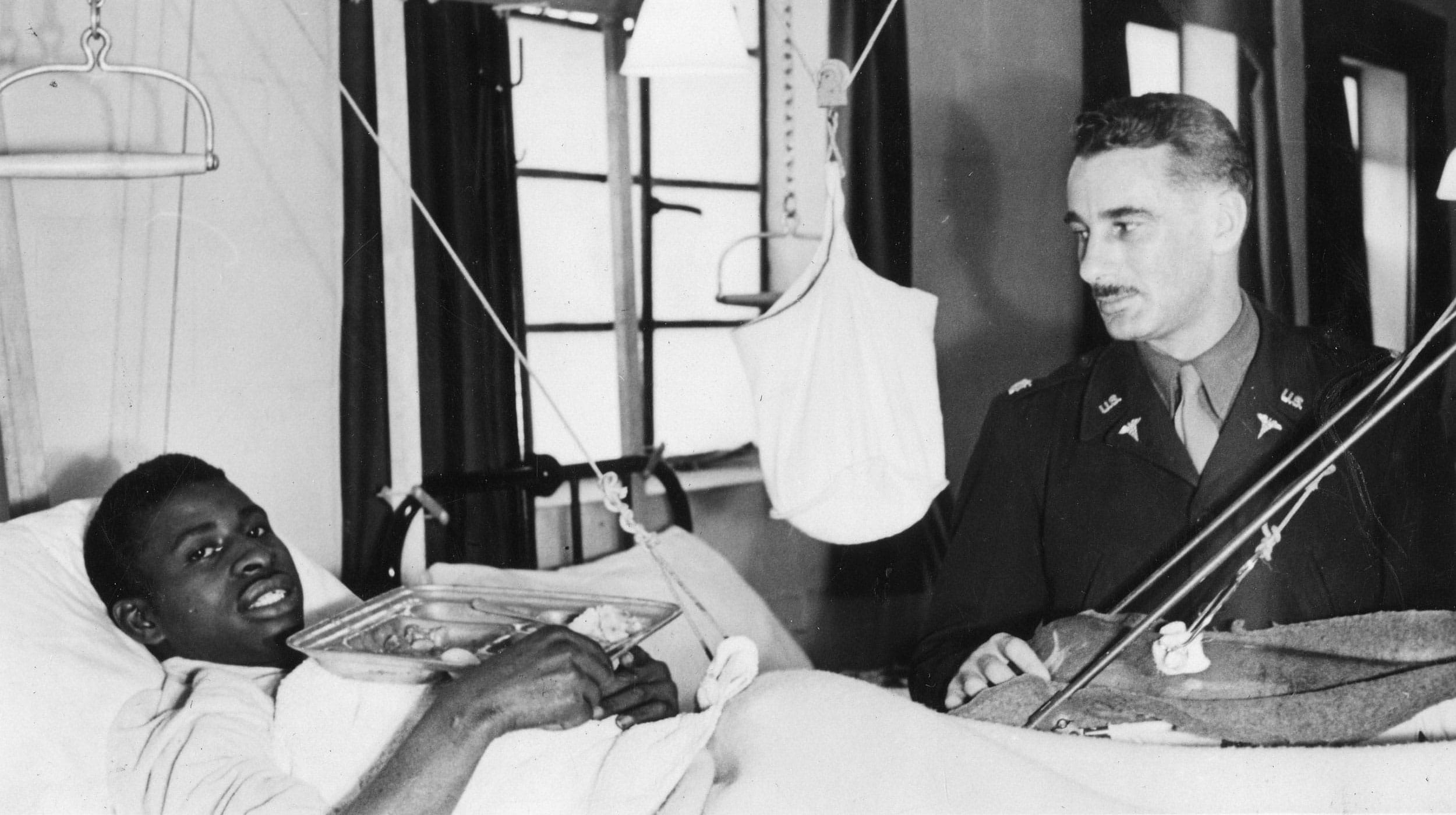 Dr. John B. Stevens visits a patient in a segregated ward at the 52nd General Hospital Unit barracks in Kidderminster U.K. (c. 1943-1945)